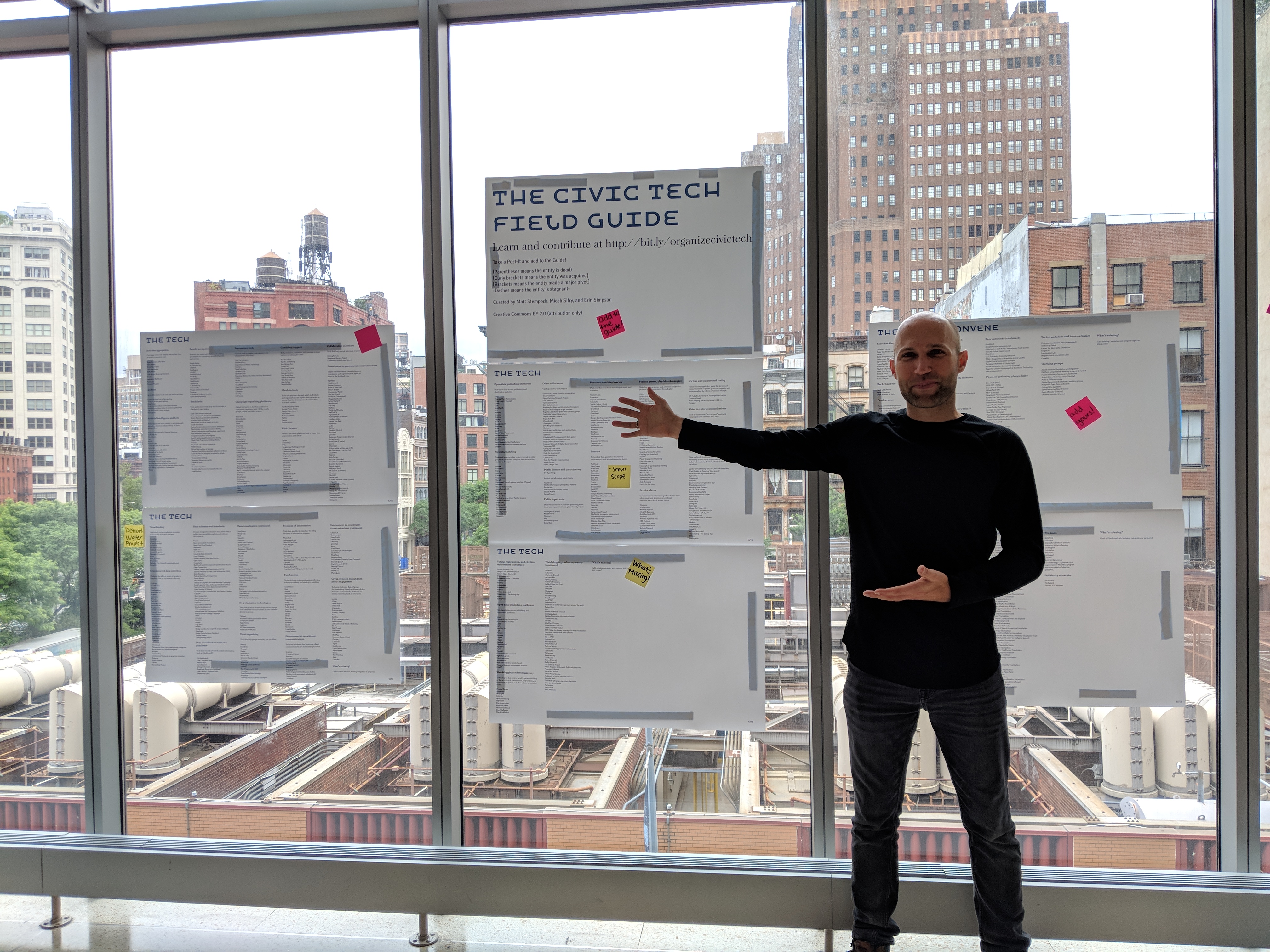 Matt stands in front of a print-out of the civic tech field guide at personal democracy forum in new york city